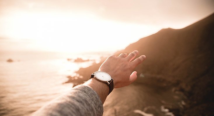 Hand Reaching Out Into Light Over Ocean and Mountain Landscape